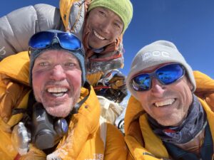 Kenton Cool, Richard Williams and Dorjee Gyelzen smile for the camera on the summit of Mount Everest with blue sky behind them