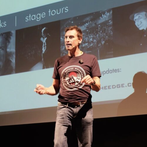 A man is pictured speaking on a stage, wearing a microphone