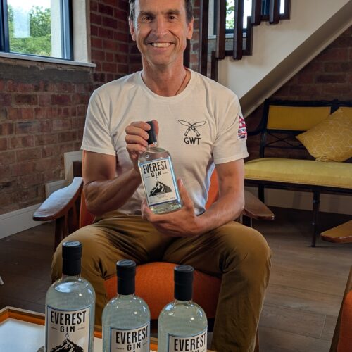A man sits holding a bottle of Everest Gin, smiling at the camera